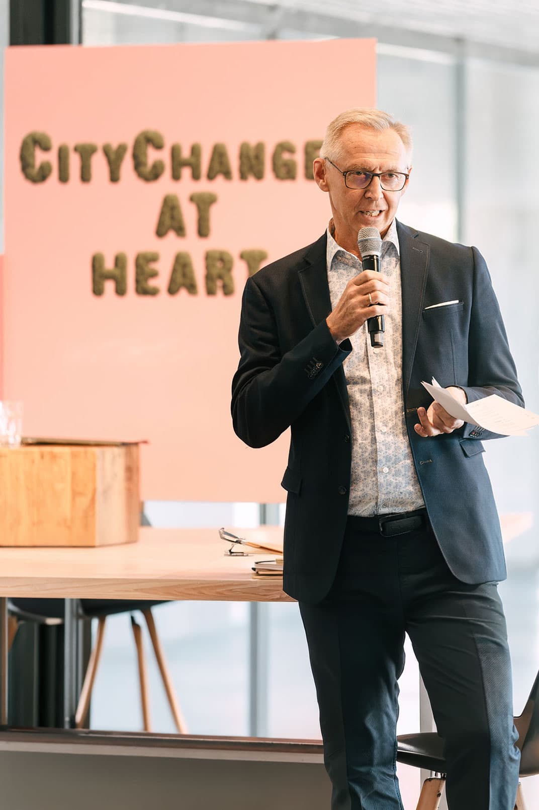 A speaker presenting at a Eurotowns event in front of a "CityChange at Heart" backdrop. The image represents the network's mission to connect medium-sized cities and drive innovation in urban resilience and development across Europe.